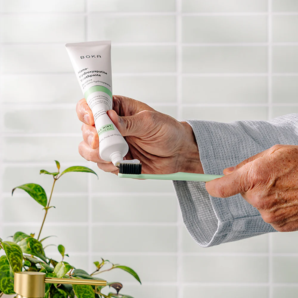 Hand squeezing Boka toothpaste onto a toothbrush
