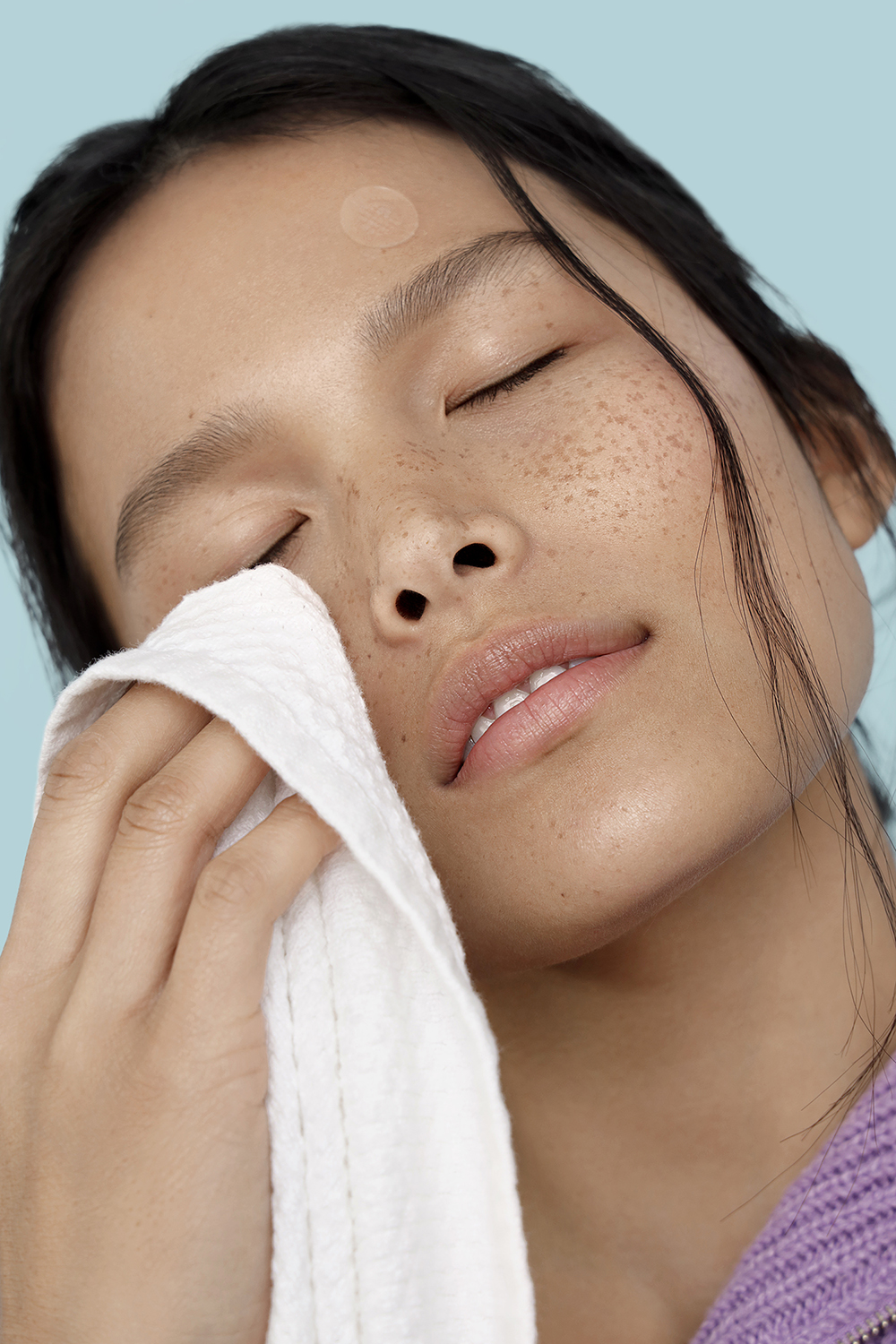 Woman with freckles drying her face with a towel