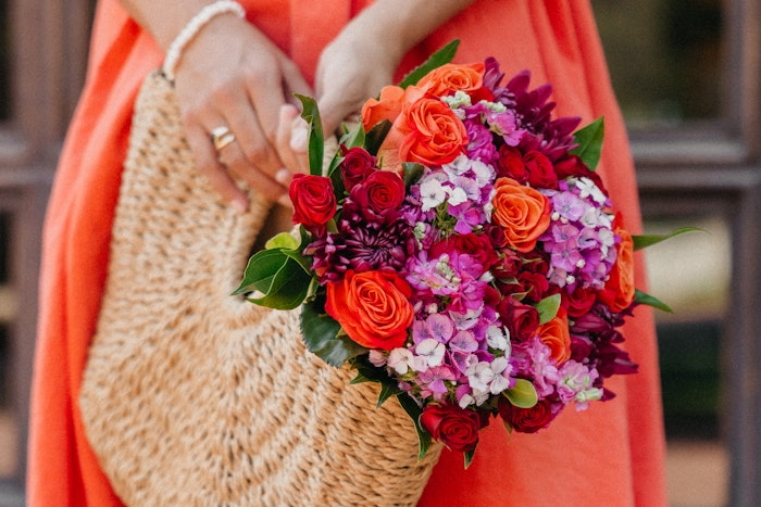 Woman holding a BloomsyBox bouquet in a straw bag