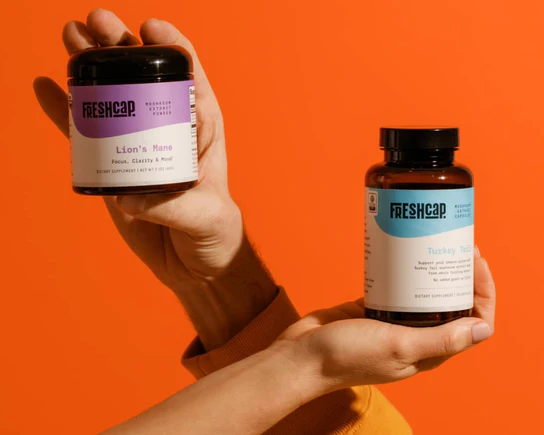 Hands holding FreshCap Lion's Mane and mushroom complex jars